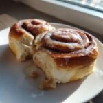 Two soft, freshly baked Holiday Eggnog Cinnamon Rolls covered in white glaze on a white plate.