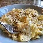 A close-up of fettuccine pasta coated in rich, creamy Homemade Alfredo Sauce, topped with grated Parmesan and black pepper.