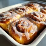 Close-up of freshly baked Homemade Orange Cinnamon Rolls covered in thick white glaze in a white baking dish.