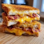 Close-up of a stacked Hot Honey Apple Cheddar Bacon Grilled Cheese sandwich with melted cheese oozing out.
