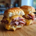 Two irresistible ham and cheese sliders stacked with melted cheese and ham on a wooden board.