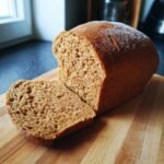 A freshly baked loaf of Irresistible Whole Wheat Bread with one slice cut, on a wooden cutting board.