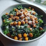 A bowl of Lemon Parmesan Kale Salad topped with crispy Hot Honey Chickpeas and grated Parmesan cheese.