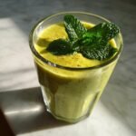 A vibrant green Mango Pineapple Matcha Mocktail topped with fresh mint leaves and a sprinkle of spice.