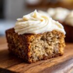 A close-up of an Irresistibly Moist Banana Bar topped with creamy swirls of cream cheese frosting.