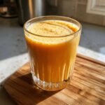 A close-up of a vibrant Orange Creamsicle Smoothie in a fluted glass, sitting on a wooden cutting board.