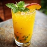 A tall glass of vibrant Passionfruit Peach Lemonade, garnished with fresh mint and a peach slice.