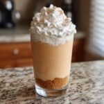 A delicious Peach Cobbler Milkshake topped with whipped cream and cinnamon, served in a glass with a graham cracker crust.