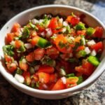 Close-up of fresh Pico De Gallo Chunky Salsa featuring diced tomatoes, onions, cilantro, and green peppers in a white bowl.
