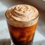 Close-up of a tall glass filled with Pumpkin Chai Cream Cold Brew, topped with whipped cream and a dusting of spice.