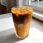 A tall, sweating glass filled with a layered Pumpkin Dirty Chai Iced Latte over ice cubes.