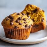 Two delicious Pumpkin Spice Chocolate Chip Muffins, one whole and one cut in half, topped with melted chocolate chips.