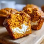 Close-up of a Pumpkin Spice Cream Cheese Muffin cut in half, revealing the bright orange crumb and creamy white center.