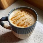 A close-up of a frothy Salted Caramel Peanut Butter Latte drizzled with caramel in a blue and beige mug.