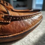 Detailed close-up of the stitching and texture of a brown leather shoe, showcasing the craftsmanship of a shoe maker.