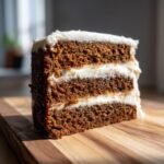 A close-up slice of Gingerbread Layer Cake With Cream Cheese Frosting showing three dark brown spiced cake layers and thick white frosting.