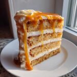 A tall slice of Southern Salted Caramel Cake with multiple layers, white frosting, and dripping caramel sauce.