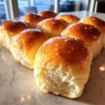 A close-up of freshly baked Soft Honey Butter Dinner Rolls, glistening with a sweet glaze and showing a fluffy interior.
