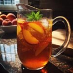 A crystal clear pitcher filled with Southern Peach Iced Tea, ice, peach slices, and a sprig of mint.