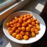 A white bowl filled with vibrant, saucy Spicy Butter Chickpeas, illuminated by natural sunlight.