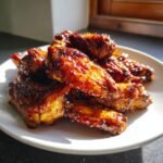 A pile of beautifully glazed Sticky Maple Apple Chicken Wings glistening under bright light on a white plate.