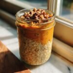 A mason jar filled with layered Sweet Potato Pie Overnight Oats, topped with chopped nuts.