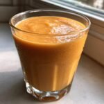 A thick, orange Sweet Potato Pie Smoothie served in a faceted glass, glistening with condensation.
