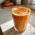 A tall glass of vibrant orange Sweet Potato Protein Smoothie, topped with a sprinkle of cinnamon.