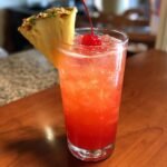 A vibrant Tia Mia cocktail with ice, garnished with a pineapple wedge and a maraschino cherry.