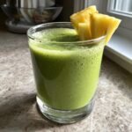A glass of vibrant green Tropical Pineapple Spinach Smoothie, garnished with fresh pineapple chunks.