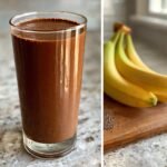 A tall glass filled with a rich Vegan Chocolate Protein Shake next to a bunch of bananas and chia seeds.