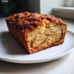 A slice of delicious Vegan Cinnamon Crunch Banana Bread on a white plate, showing the moist crumb and cinnamon swirl.