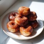 A stack of glistening, cinnamon-sugar coated Vegan Gingerbread Donut Holes piled on a small white plate.
