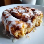 Close-up of a fluffy Vegan Pumpkin Cinnamon Rolls drizzled generously with white icing on a white plate.