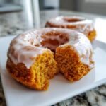 Close-up of a Vegan Pumpkin Donut With Glaze broken in half, showing the moist, orange crumb texture.