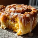 A close-up of a soft Vegan Sweet Potato Cinnamon Roll topped with maple pecan glaze and white icing dripping down the side.