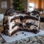A slice of decadent Vegan Vanilla Oreo Cake showing layers of dark chocolate cake and creamy vanilla frosting with crushed Oreos.