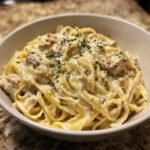 A close-up of a bowl of Weeknight Creamy Chicken Alfredo pasta, featuring fettuccine noodles, chicken pieces, and a rich, creamy sauce, garnished with parsley and Parmesan cheese.