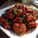 Close-up of glossy, deep-red 30 Minute Szechuan Chicken Spicy Delight pieces garnished with dried chilies and fresh green herbs.