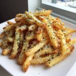 A mound of golden, crispy Air Fryer Garlic Parmesan French Fries topped with grated cheese and parsley.