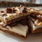 Stacked squares of no-bake Cheesecake Bark featuring a thick graham cracker crust and white chocolate topping with chocolate chunks.