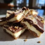 Close-up stack of layered Cheesecake Bark squares showing graham cracker crust, creamy filling, and chocolate topping.