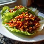 Close-up of savory Chicken Lettuce Wraps served on crisp iceberg lettuce cups on a white plate.