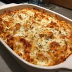 Close-up of a bubbling Chicken Pasta Bake topped with melted, golden-brown cheese and herbs.