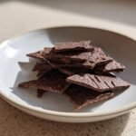 A small pile of broken, dark, textured Chocolate Crackers pieces resting in a light-colored bowl.