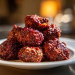 A close-up of a pile of glazed Cranberry BBQ Jerk Meatballs glistening with sauce on a white plate.
