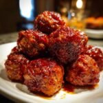 Close-up of a mound of sticky, glazed Cranberry BBQ Jerk Meatballs piled high on a white plate.