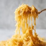 Close-up of creamy spaghetti squash strands being lifted and stretched by a fork, showing its texture.