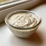 A close-up of creamy Vanilla Chia Pudding in a clear glass bowl, showing the texture and seeds.