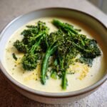 A bowl of creamy vegan white bean soup topped with bright green saut&eacute;ed broccolini florets.